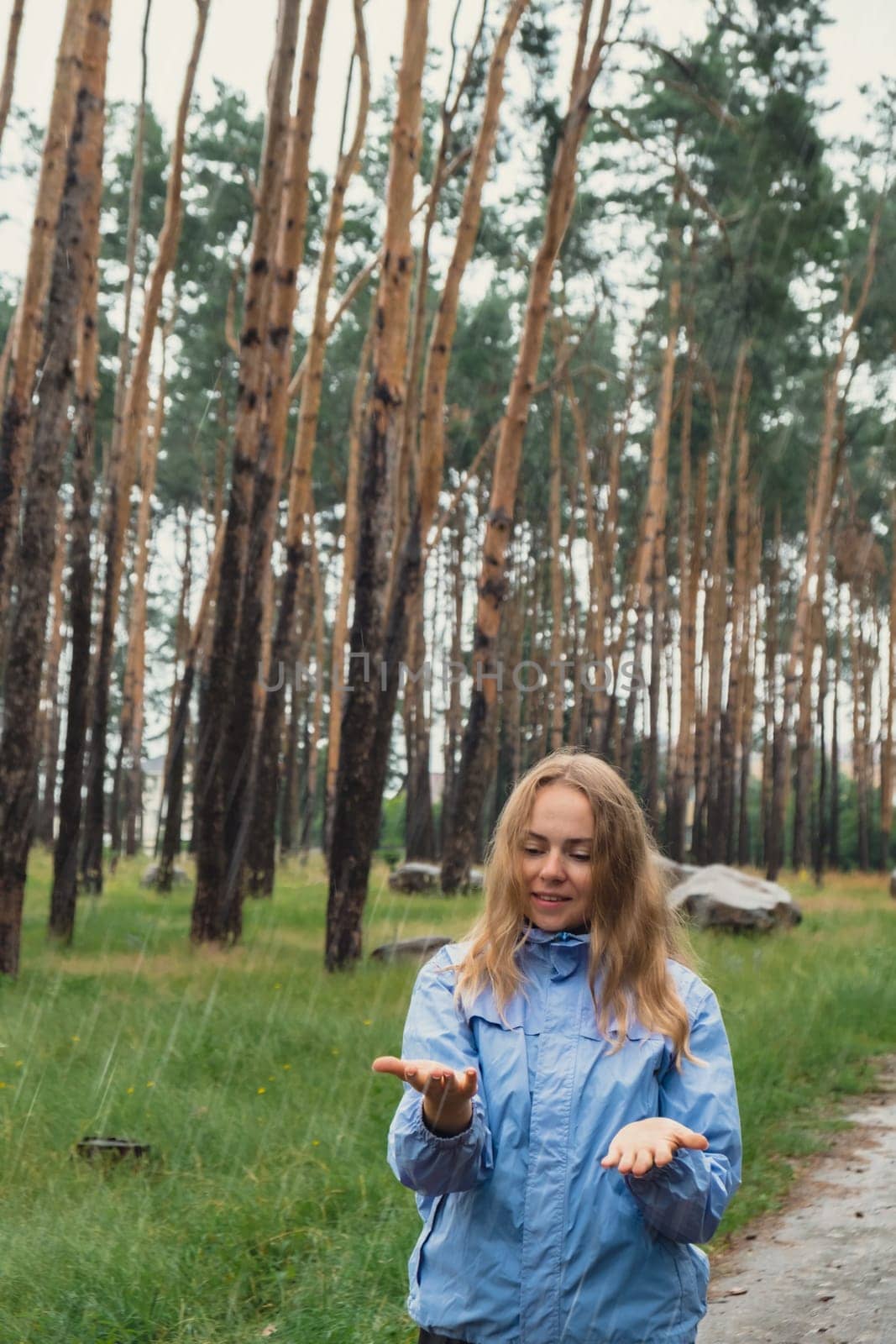 Happy young woman in blue raincoat enjoying the woods in park. True emotions open arms outdoors in rainy weather forecast. Tourist rest and feel freedom. Autumn season