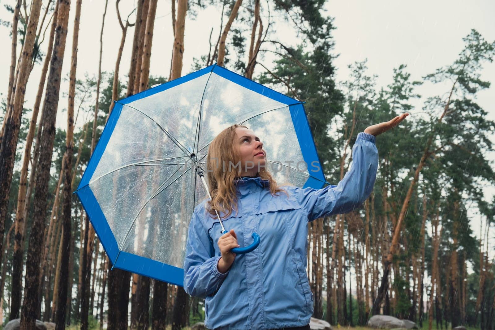 Blonde girl checking the weather under transparent umbrella outside in park. Autumn time rainy bad forecast conditions season. Tourist with umbrella travel in new places in rain by anna_stasiia