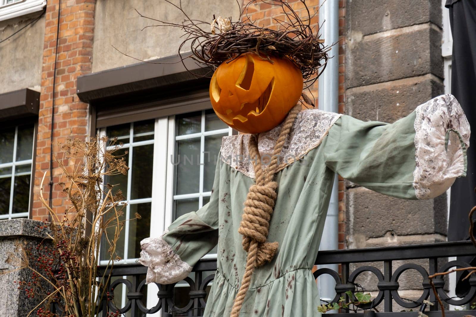 Exterior Beautiful atmospheric halloween scary scarecrow pumpkin decorated on porch. Autumn leaves and fall flowers celebration holiday Thanksgiving October season outdoors by anna_stasiia