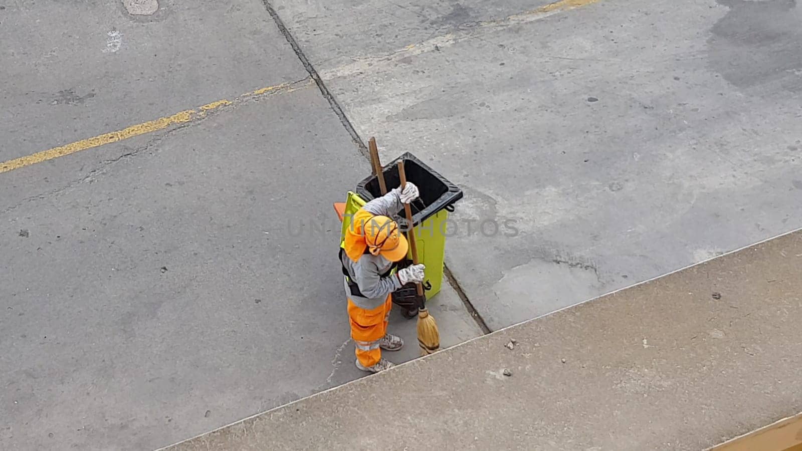 Top view of a worker cleaning the sidewalk of the street sweeping the garbage. Public maintenance concept. by Peruphotoart