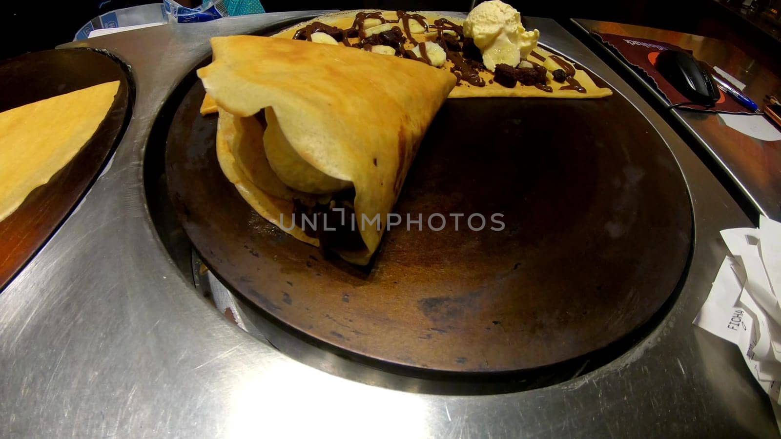Scrumptious folded crepe topped with chocolate syrup and a scoop of vanilla ice cream, served on a rustic hot plate