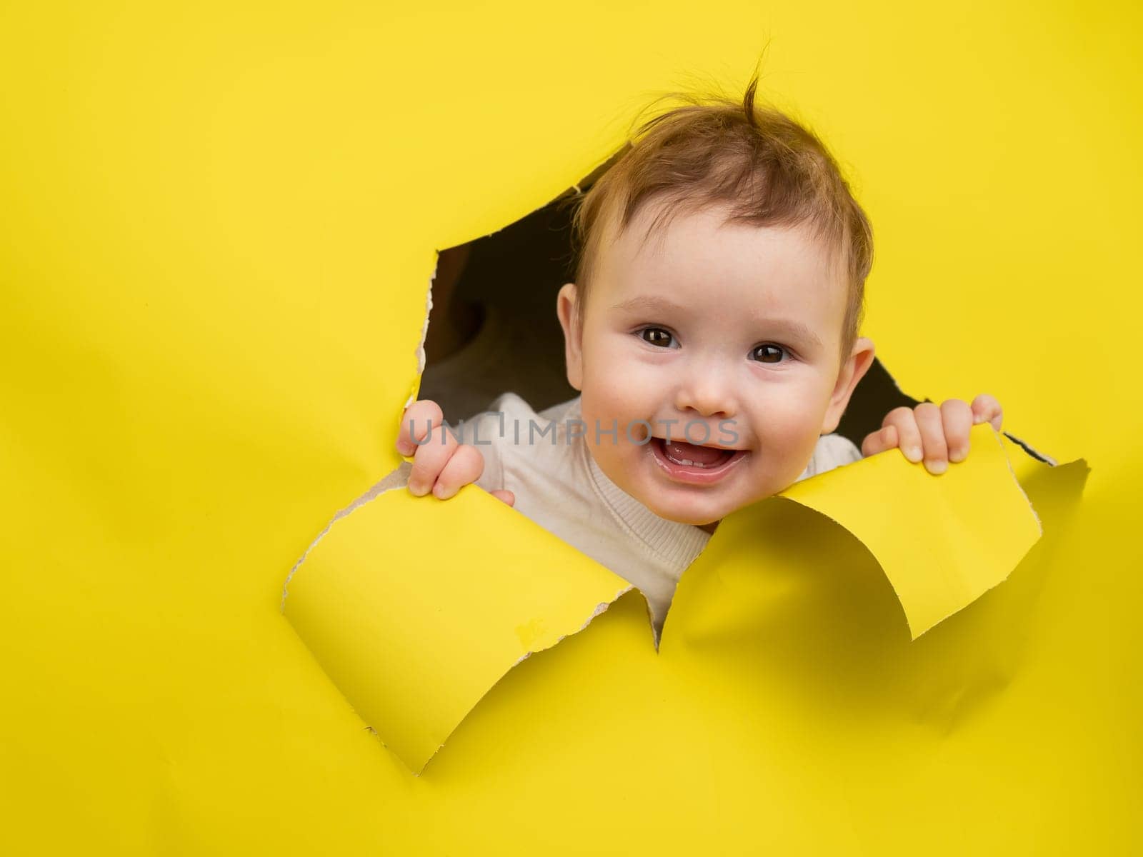 Cute Caucasian baby sticking out of a hole in a paper yellow background. by mrwed54