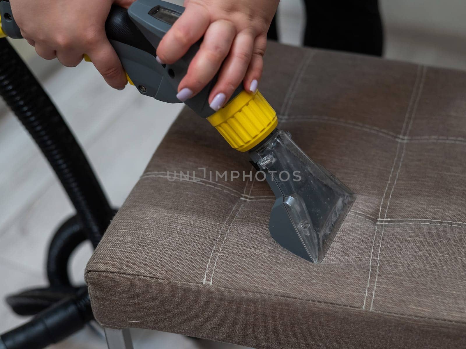 Woman cleaning a fabric chair with a professional washing vacuum cleaner. by mrwed54