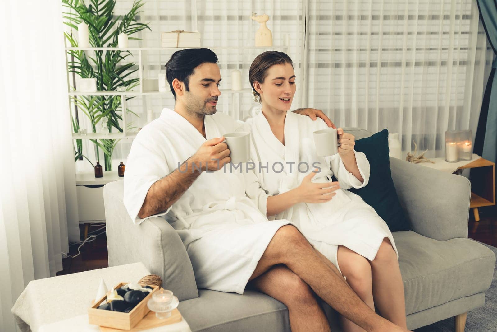 Beauty or body treatment spa salon vacation lifestyle concept with couple wearing bathrobe relaxing with drinks in luxurious hotel spa or resort room. Vacation and leisure relaxation. Quiescent