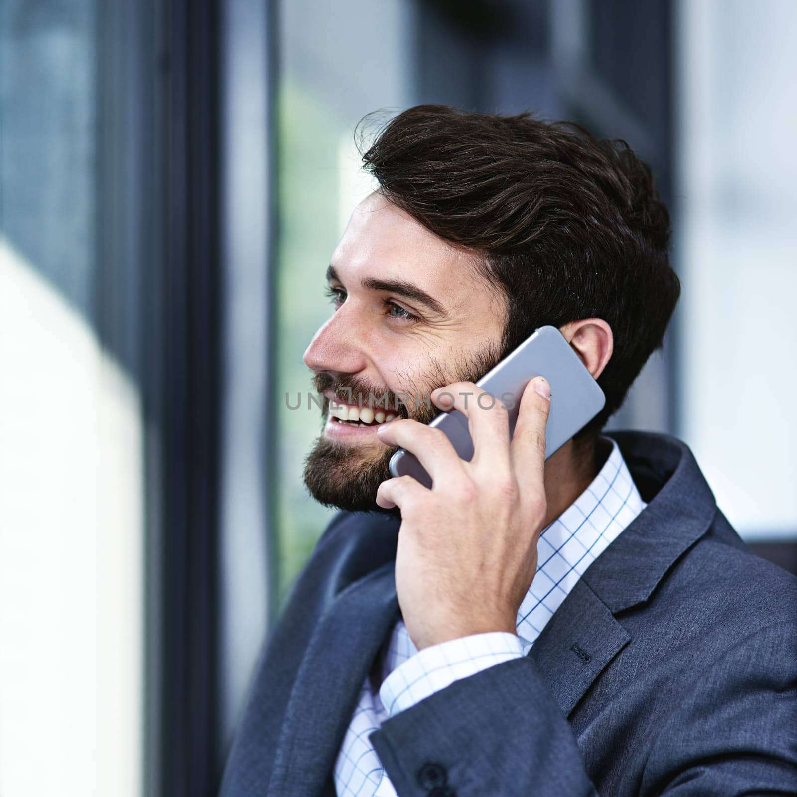 Happy, businessman and phone call with discussion for chat, proposal or communication by window at office. Young man or employee talking on mobile smartphone with smile for business conversation.