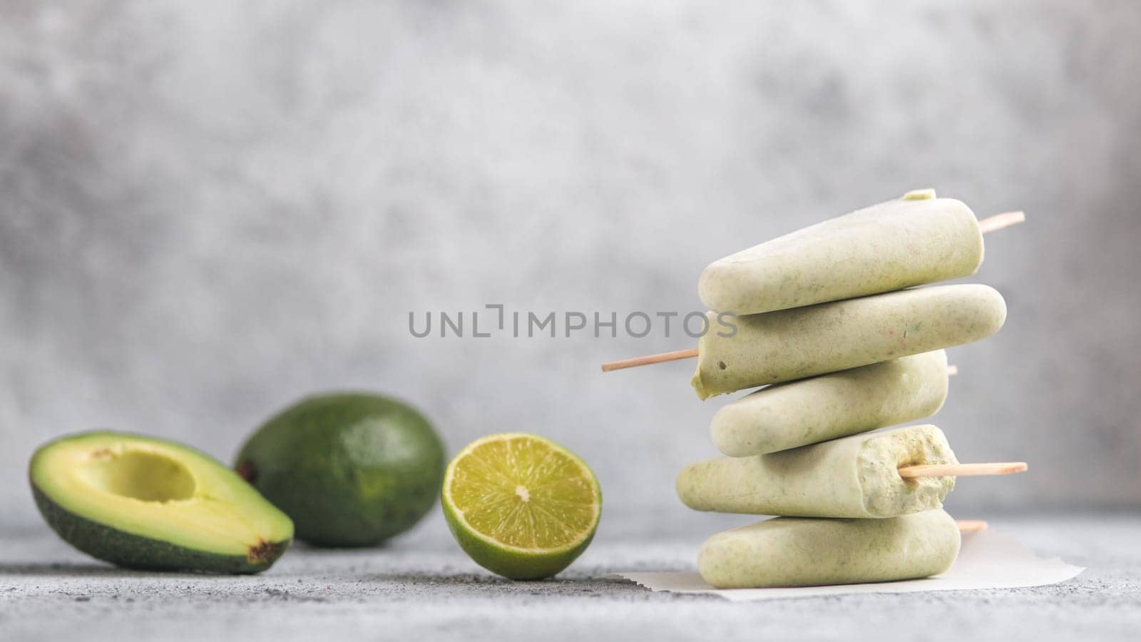 Homemade raw vegan avocado lime popsicle. Sugar-free, non-dairy green ice cream on gray cement textured background. Copy space. Ideas and recipes for healthy snack, dessert or smoothie. Banner
