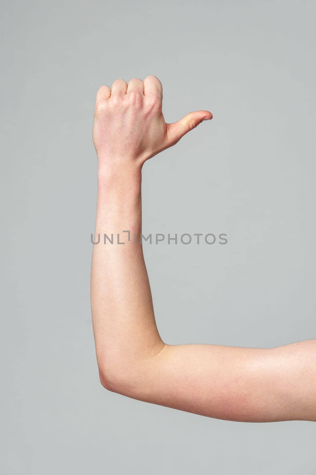 A persons forearm is shown flexed at the elbow with the fist clenched, highlighting the muscles and tendons of the human arm. The forearm is positioned against a neutral gray backdrop, emphasizing the anatomy and physical fitness.