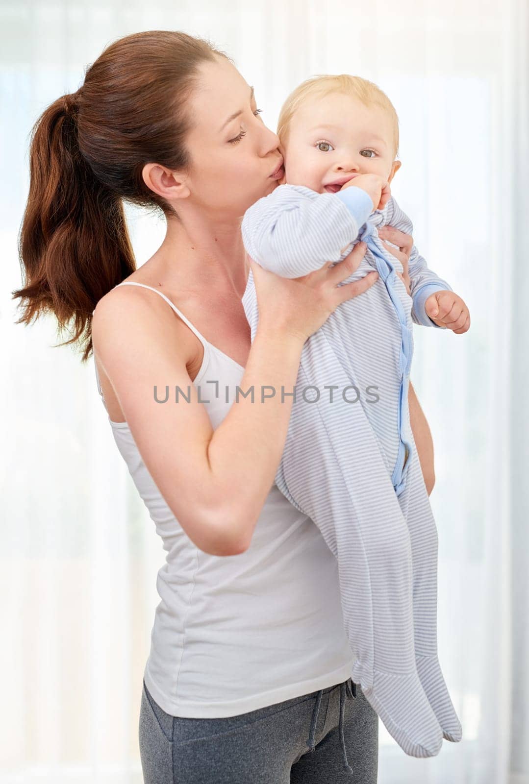 Family, love and mother kissing baby in home together for morning bonding, relationship or trust. Bedroom, growth and kids with young woman holding infant in apartment for care or child development by YuriArcurs