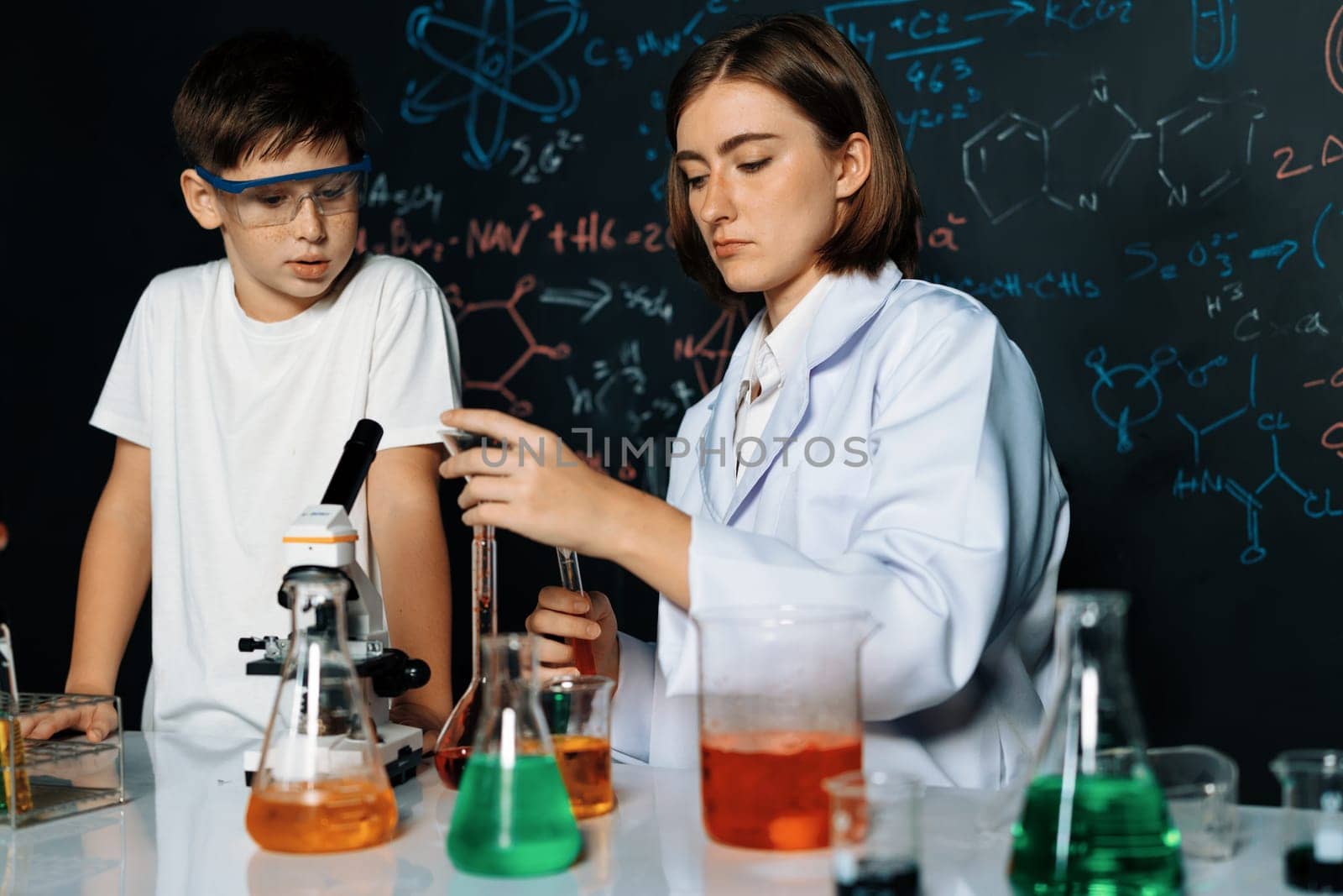 Teacher support schoolboy in laboratory. Schoolboy and teacher stand and experiment about science of chemistry in STEM class using liquid in glass container. Instructor mixing solution. Erudition.