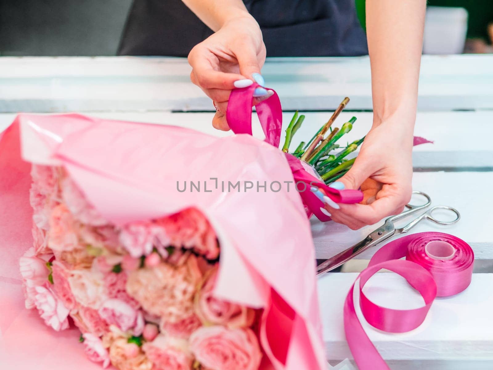 Florist hands collect bouquet of flowers in studio. Florist creating order, making rose, peony and tulip bouquet in flower shop. Florist are doing bouquet. Florist at work. Copy space