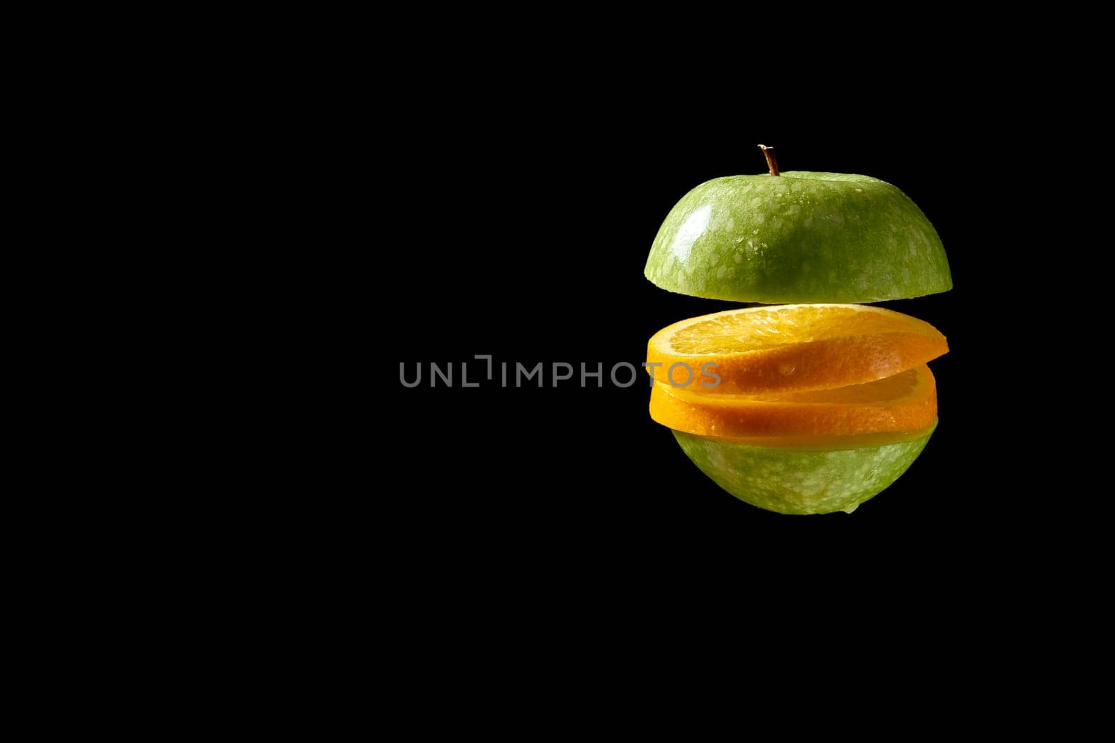 Close up of sliced green organic fresh apple and orange with water droplets on black background