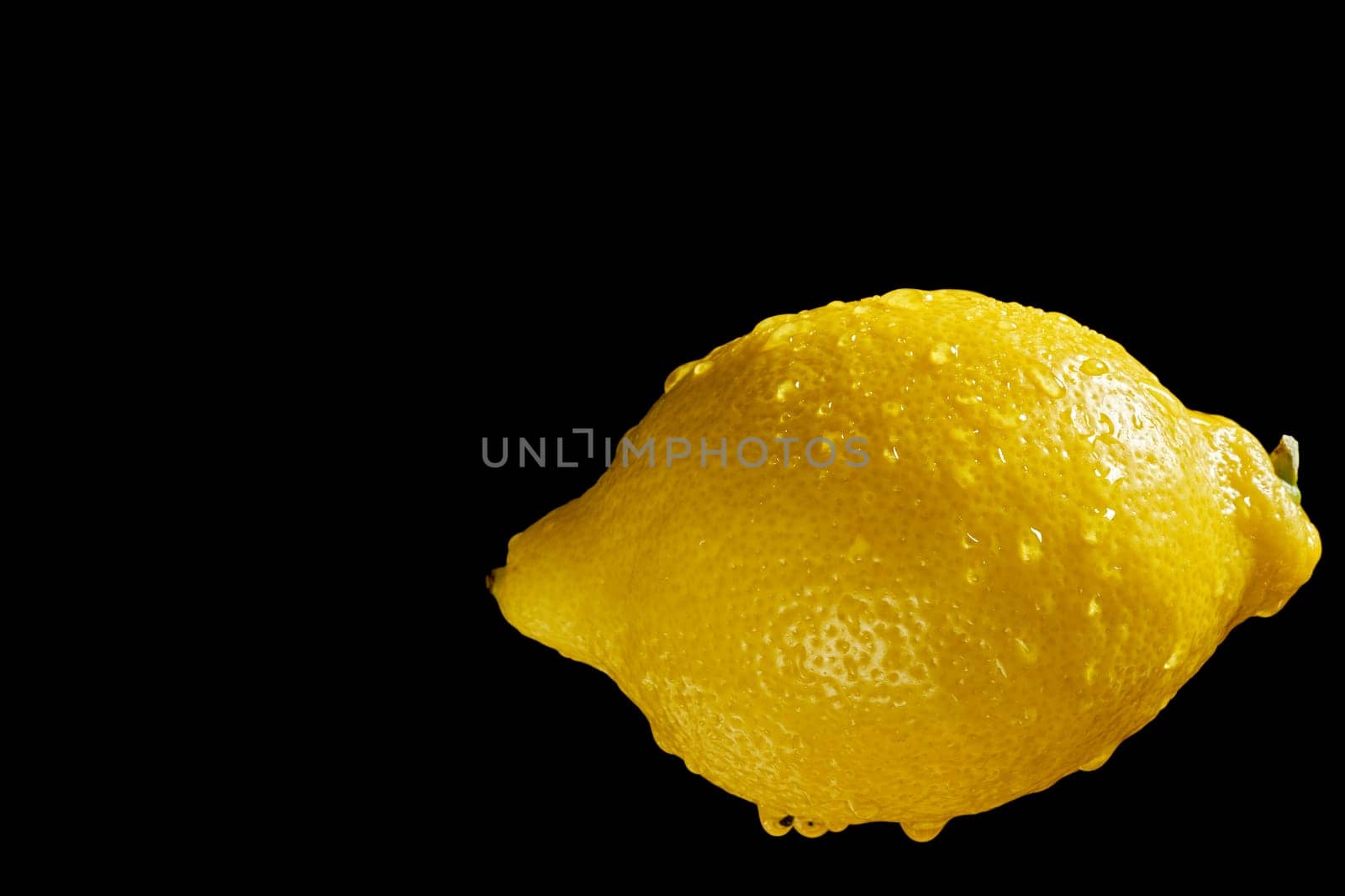 Close up of fresh yellow organic lemon with water droplets on black background