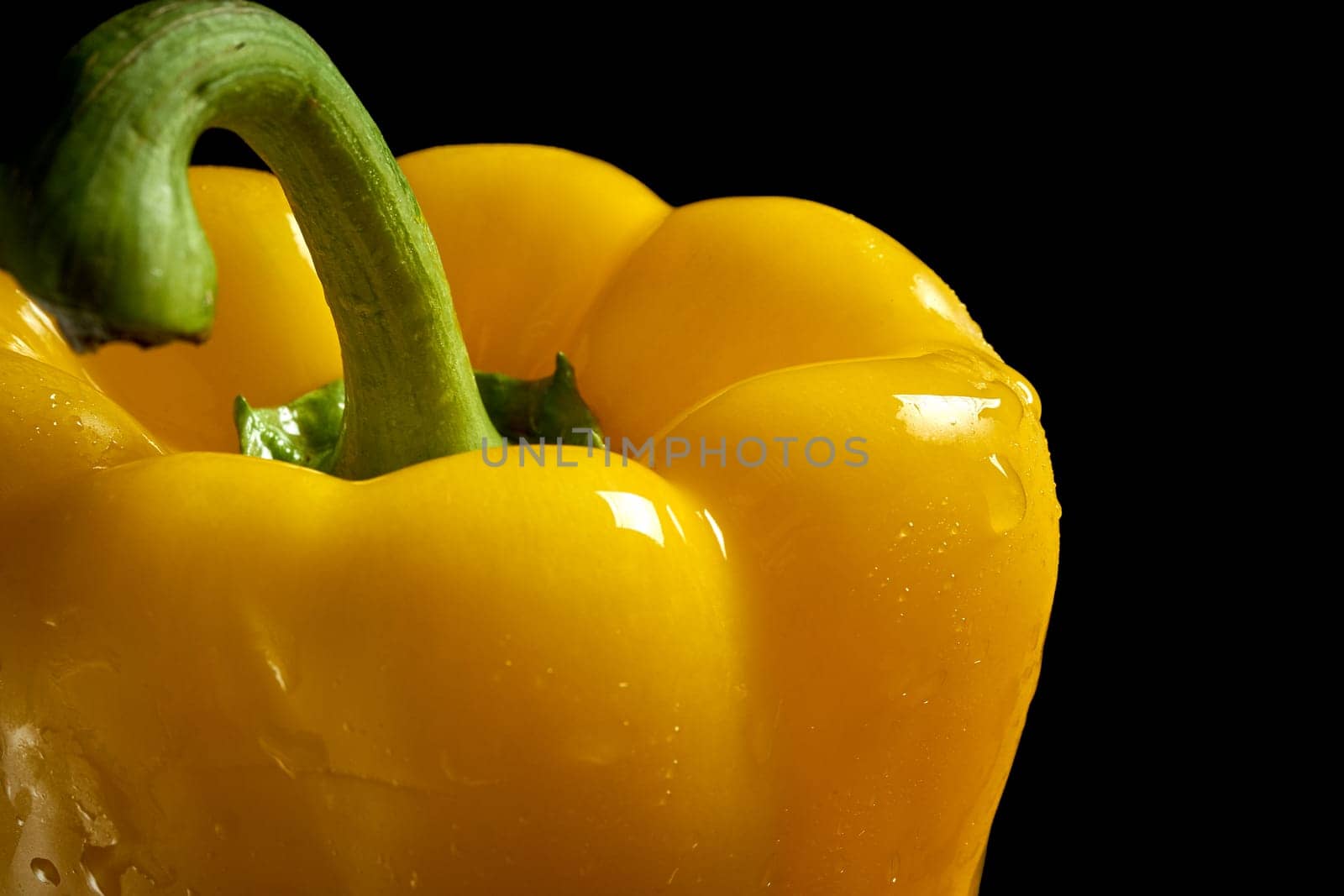 Closeup of yellow fresh organic pepper with drops of water on black background