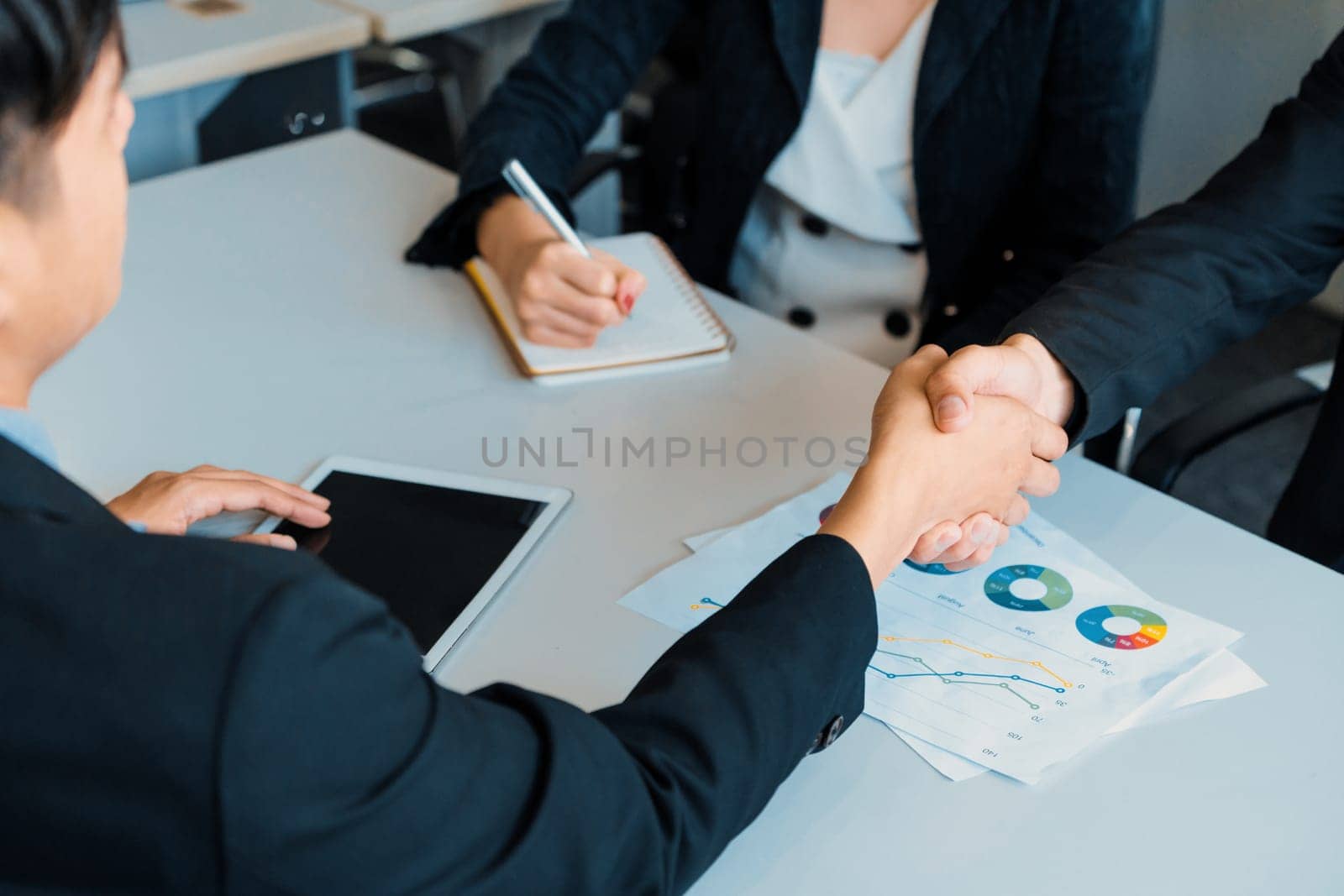 Business people agreement concept. Asian Businessman do handshake with another businessman in the office meeting room. Young Asian secretary lady sits beside him. uds