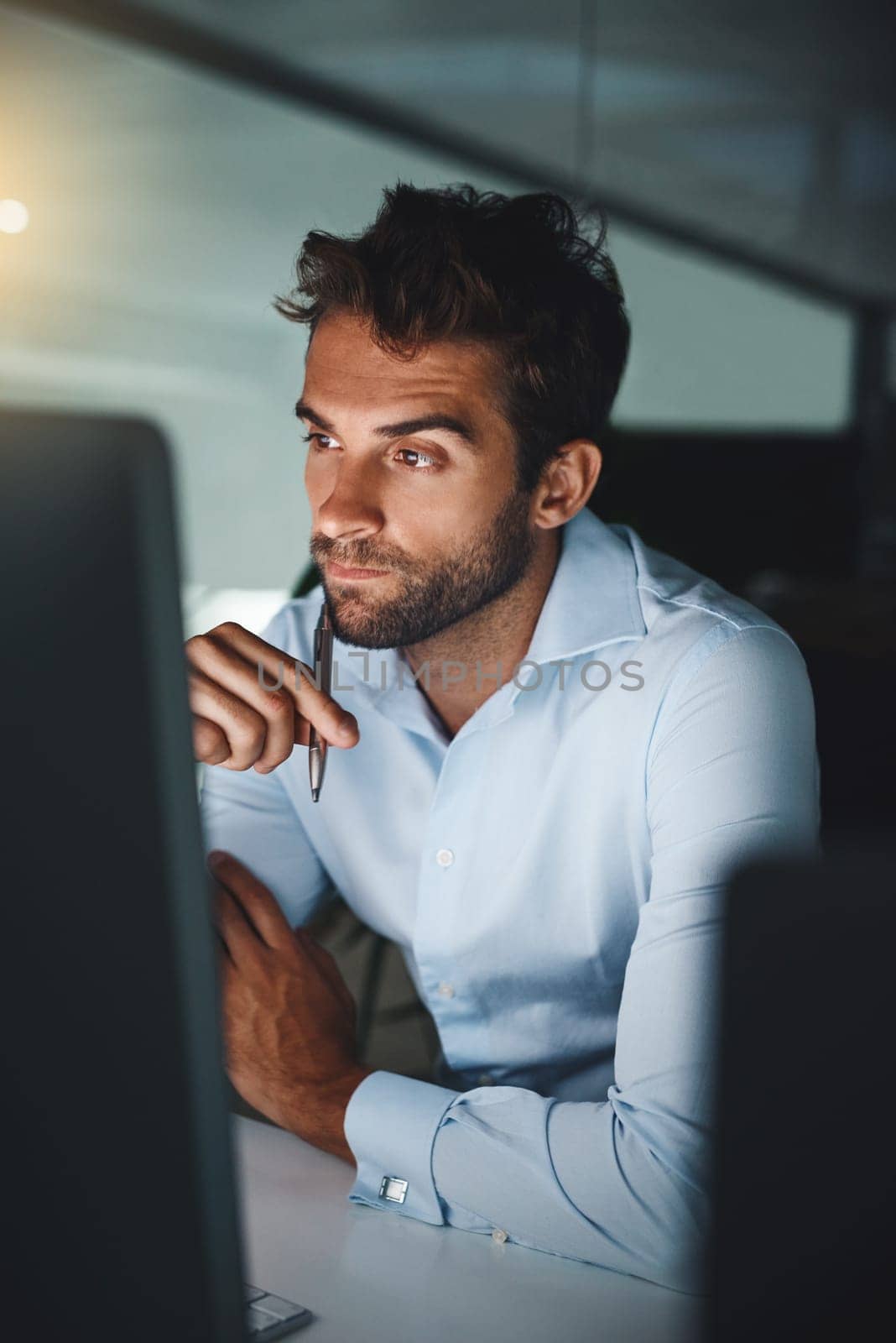 Serious, thinking and businessman with pen by computer for email, internet and working late in office for corporate career. Happiness, desk and lawyer with technology for communication in workspace.