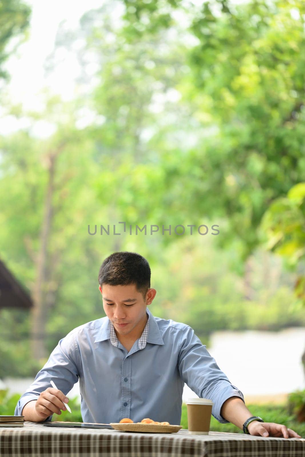 Portrait of young businessman in smart casual wears using digital tablet at outdoor cafe.