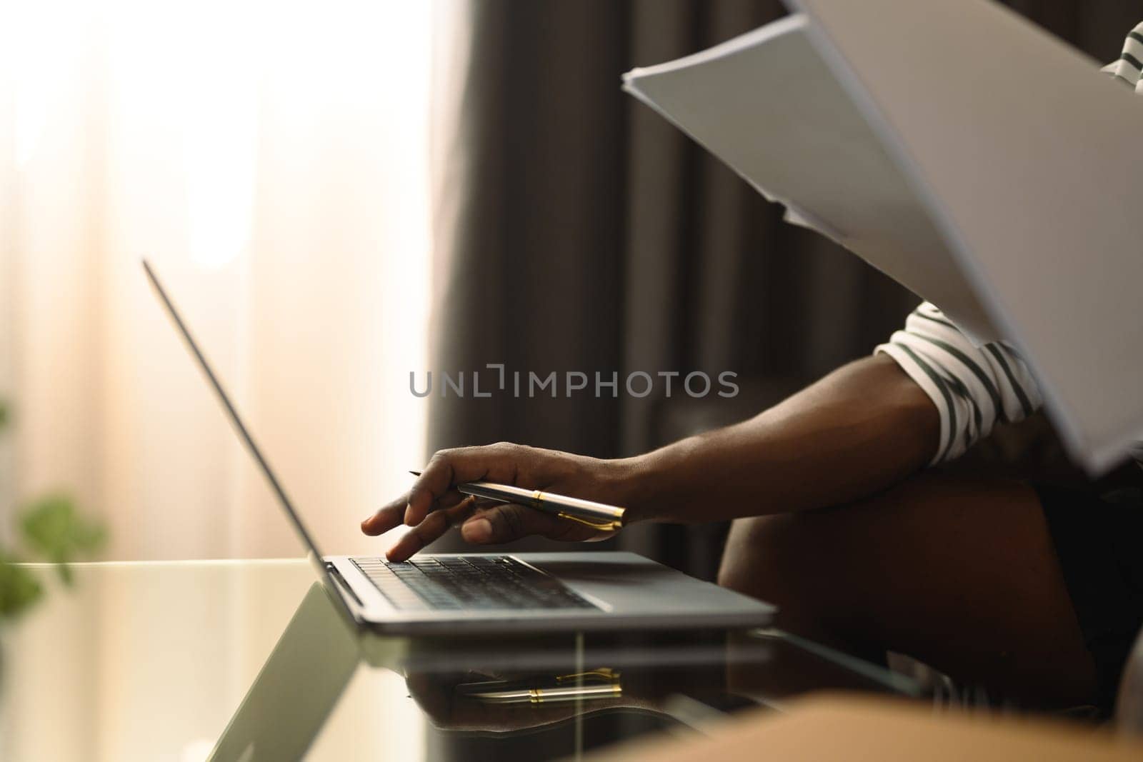 Cropped shot African millennial man freelancer sitting on couch and working with laptop by prathanchorruangsak