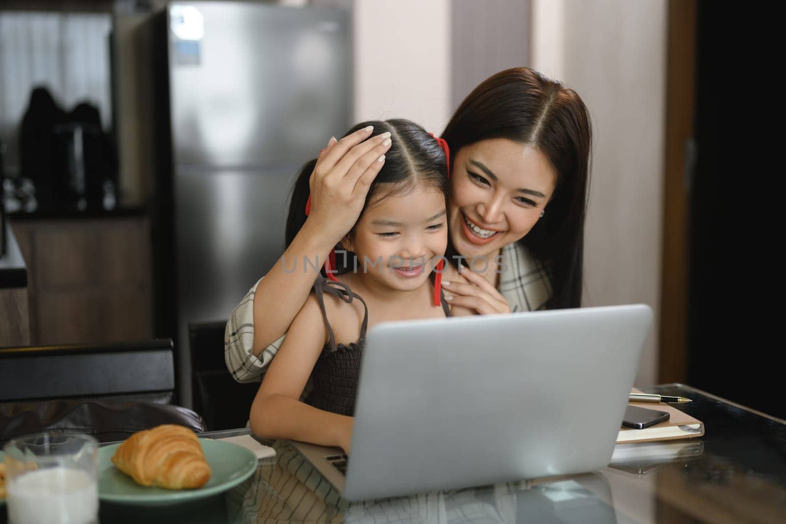 Beautiful working mom using a laptop and spending time with her little daughter at home by prathanchorruangsak