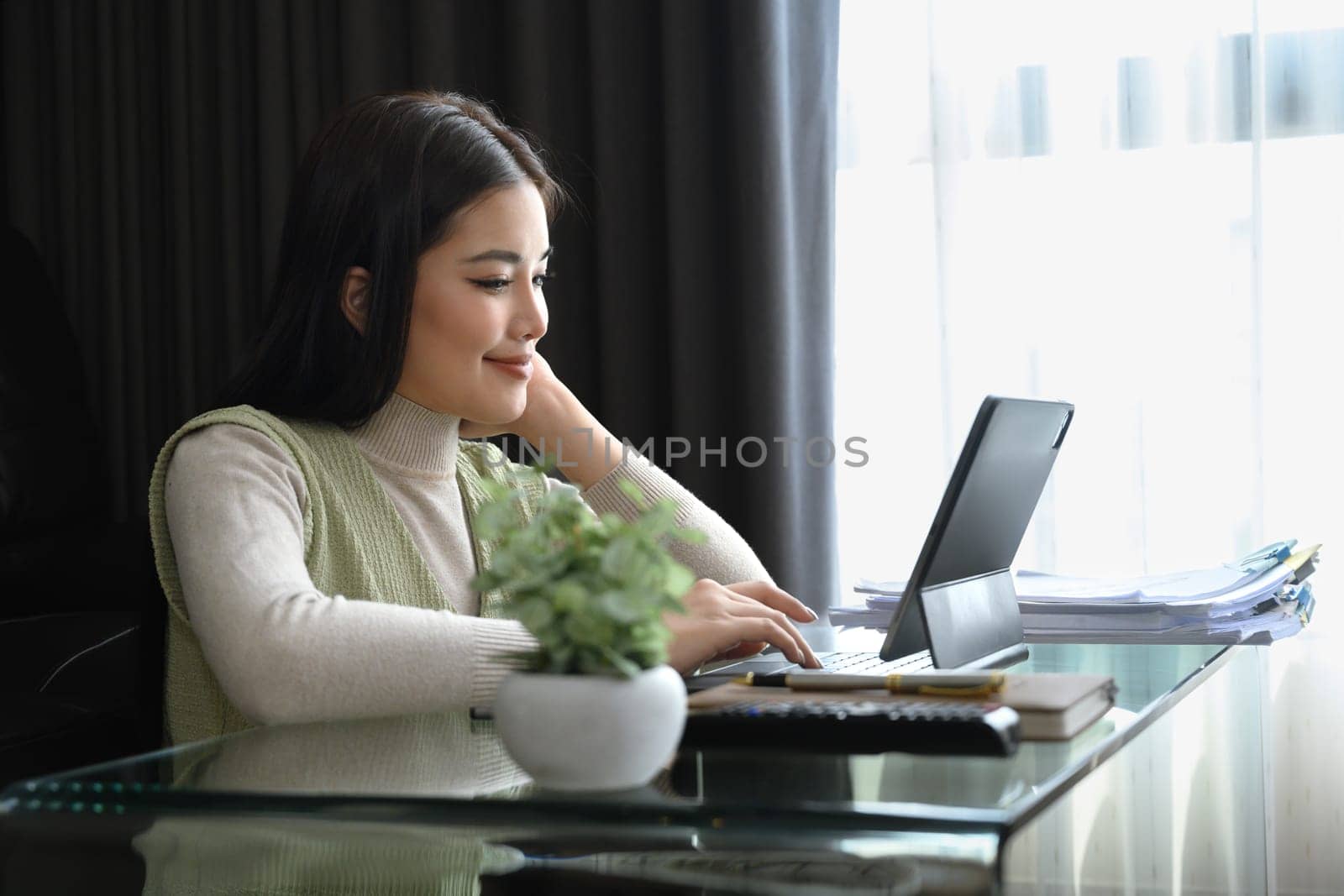 Young businesswoman sitting in modern living room and working with laptop. Remote work concept by prathanchorruangsak