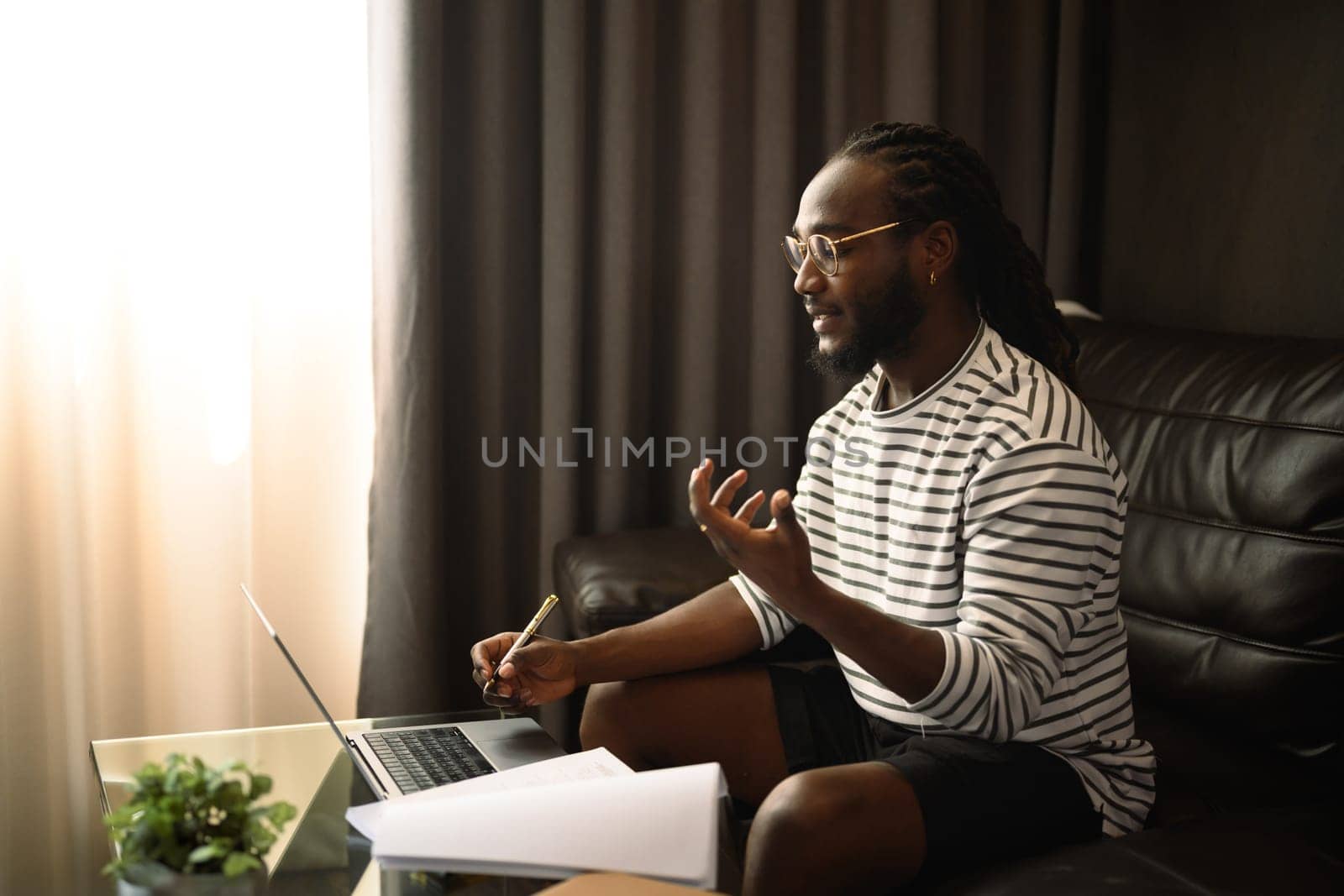 Smiling young African man freelancer having video call on laptop during working at home by prathanchorruangsak