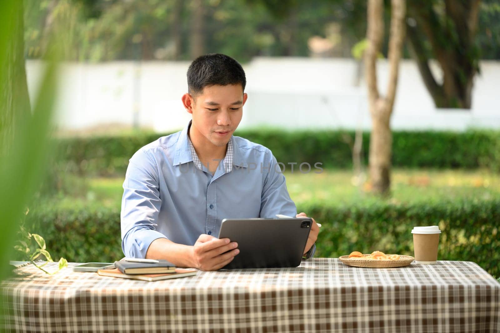 Portrait of young businessman in smart casual wears using digital tablet at outdoor cafe by prathanchorruangsak