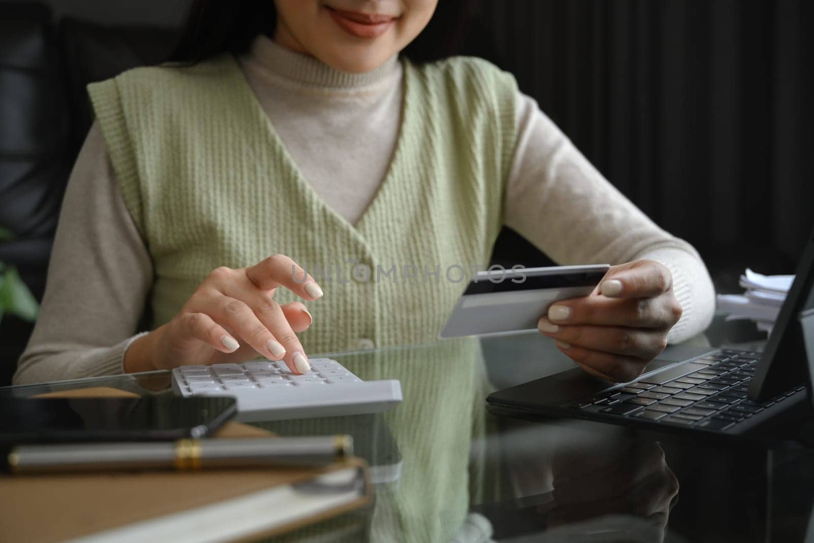 Cropped shot young woman holding credit card and calculating expenses at home.