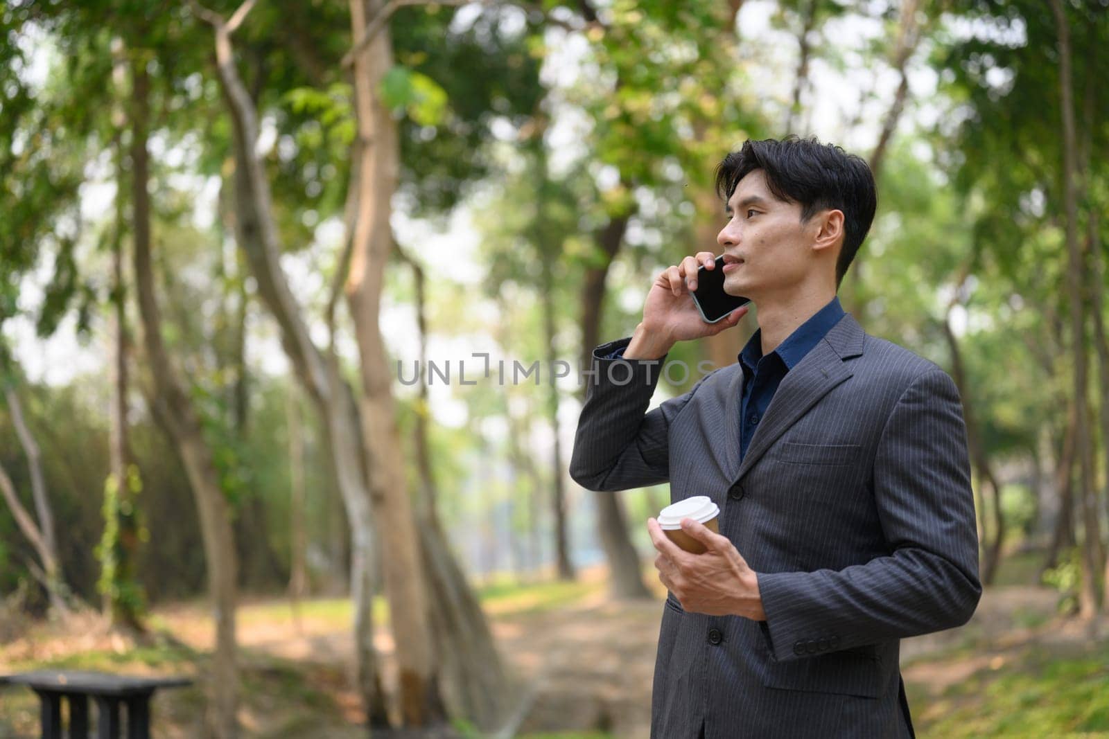 Handsome young businessman talking on mobile phone while standing at urban park.