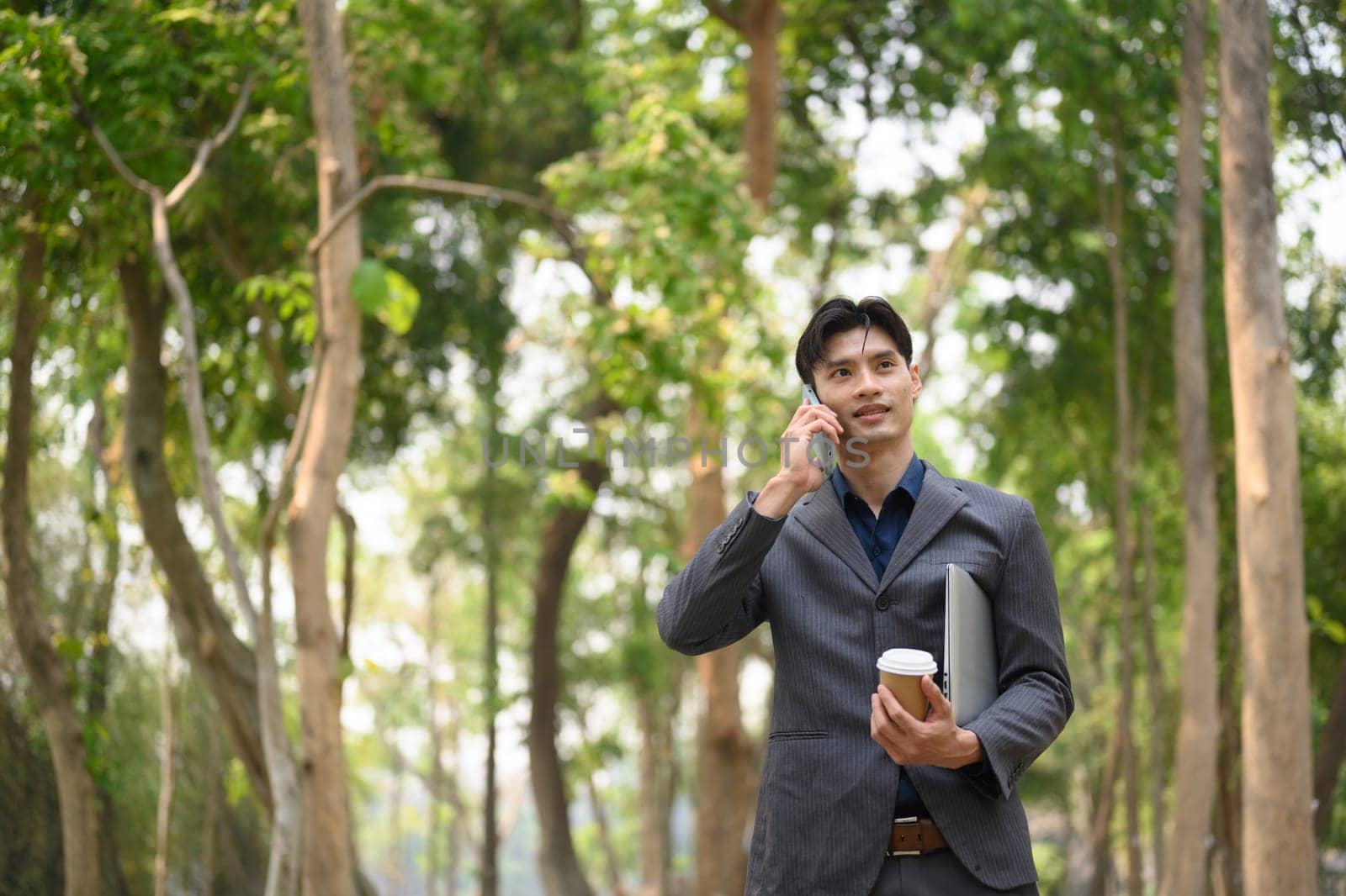 Handsome young businessman talking on mobile phone while standing at urban park.