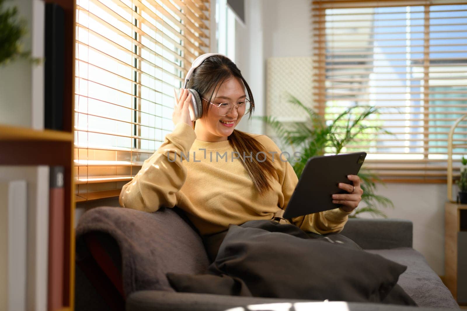 Cheerful teenage asian girl wearing headphone watching video on digital tablet by prathanchorruangsak