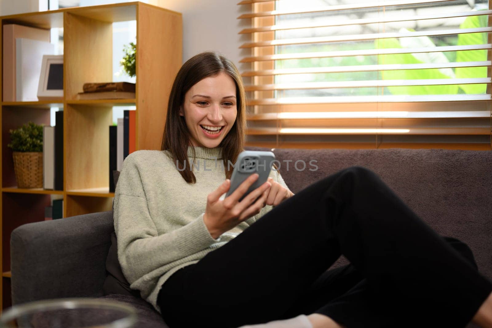 Relaxed caucasian woman sitting on couch at home and using mobile phone by prathanchorruangsak