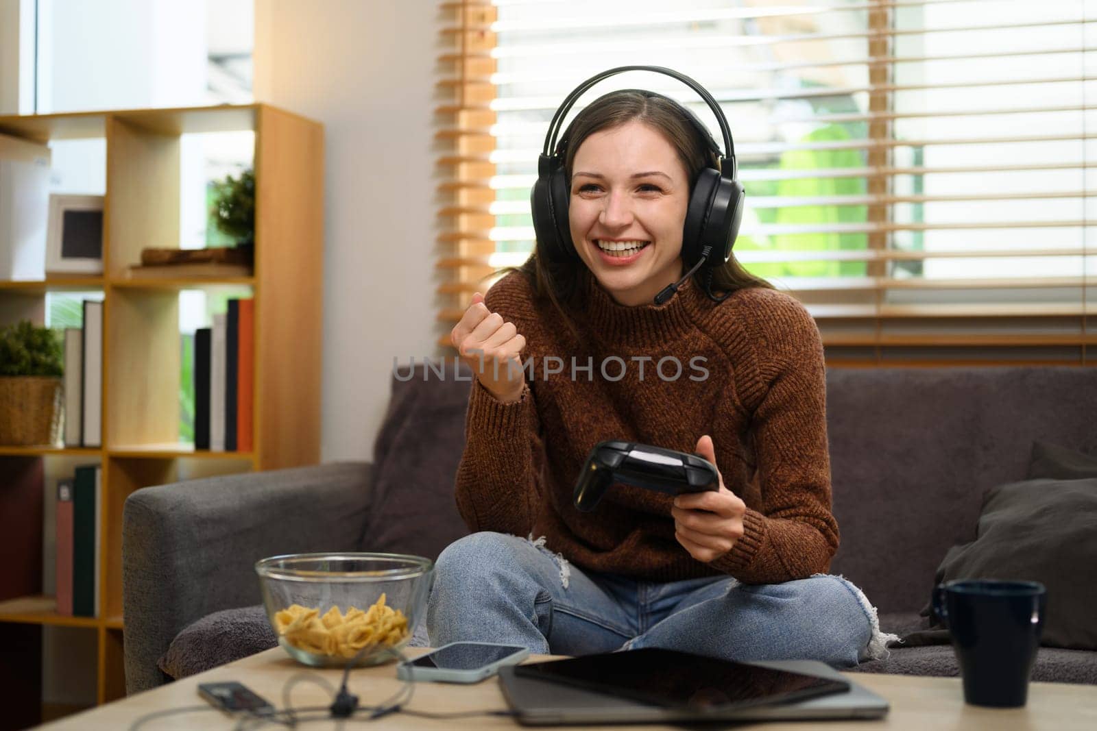 Happy young woman with joystick celebrating victory in online video game by prathanchorruangsak