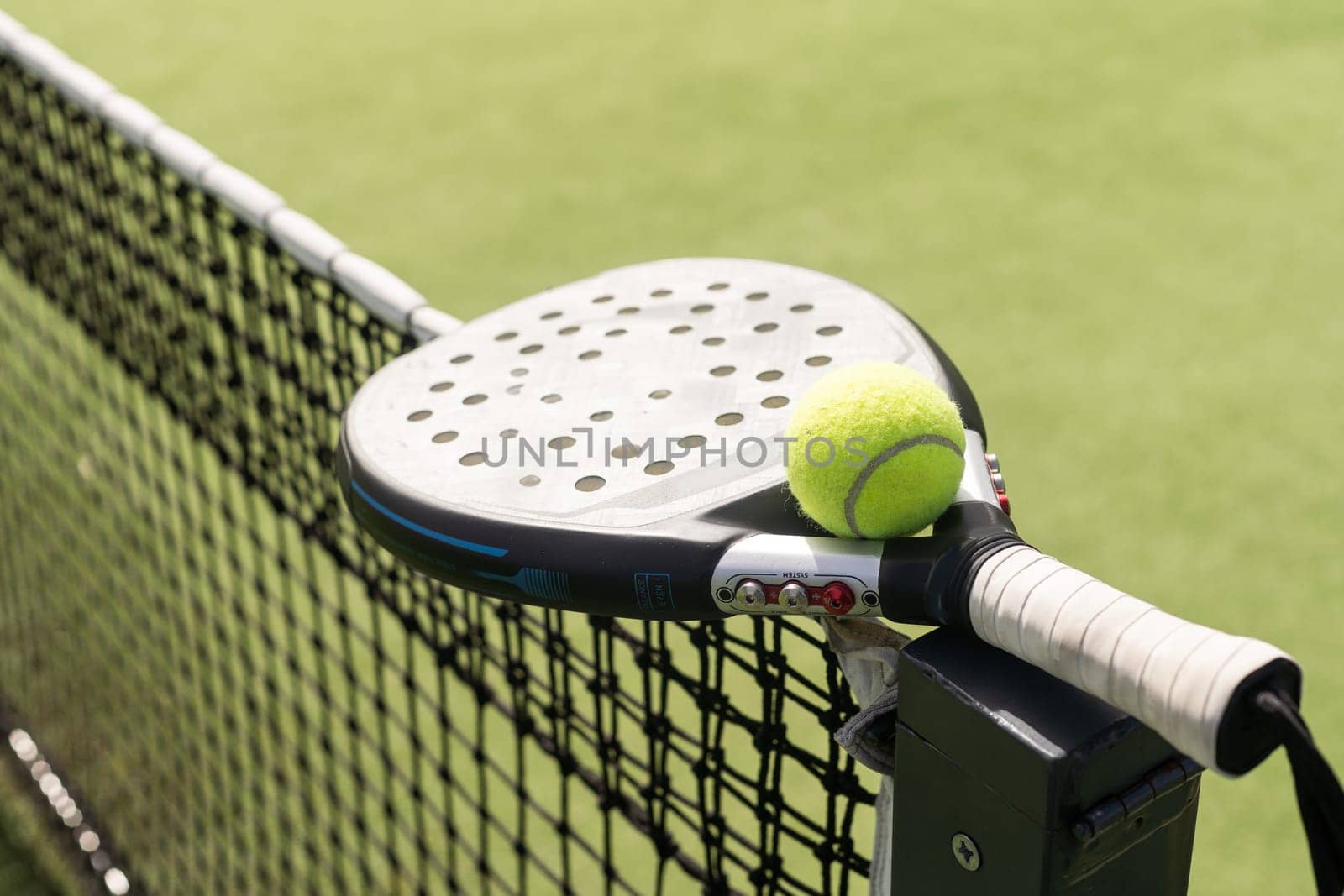 Padel racket and padel ball on a green court in the sunset. High quality photo