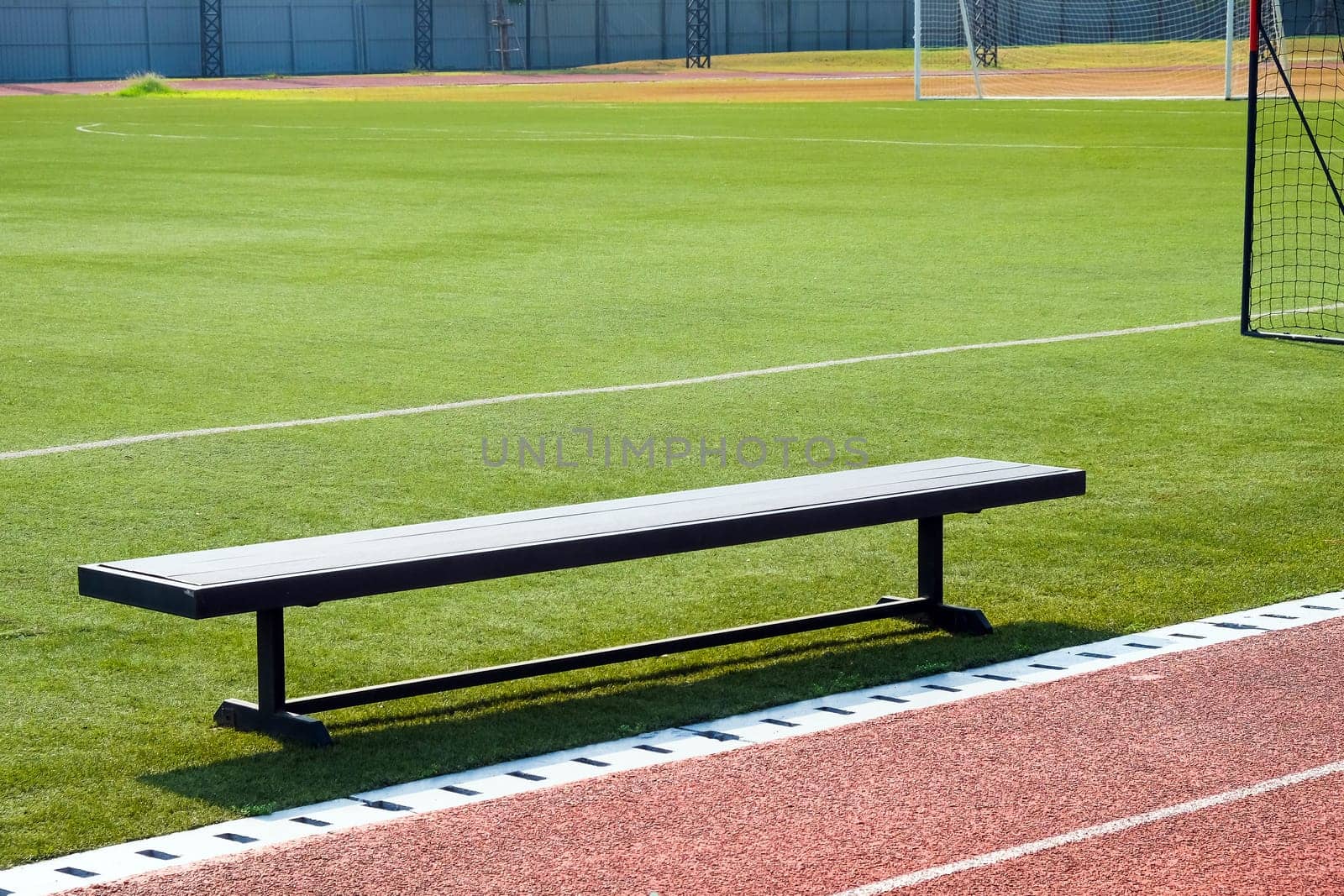 Empty bench on the sports field with green grass and red running track by ponsulak