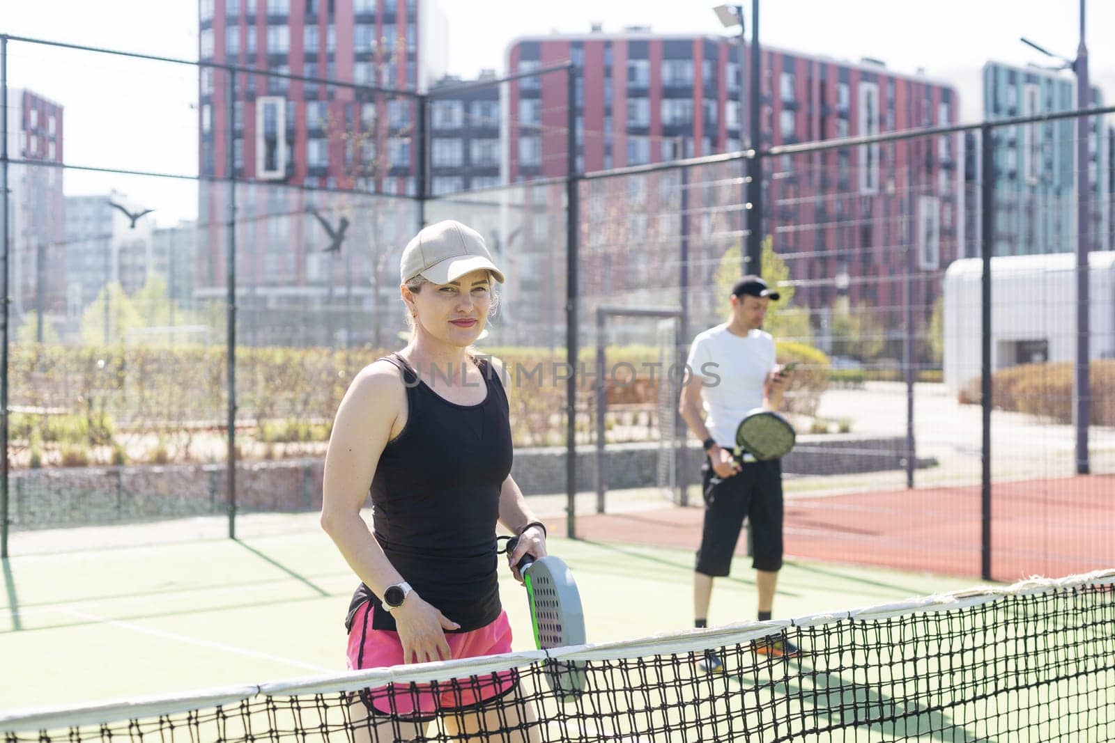 Portrait of positive young woman and adult man standing on padel tennis court, holding racket and ball, smiling. High quality photo