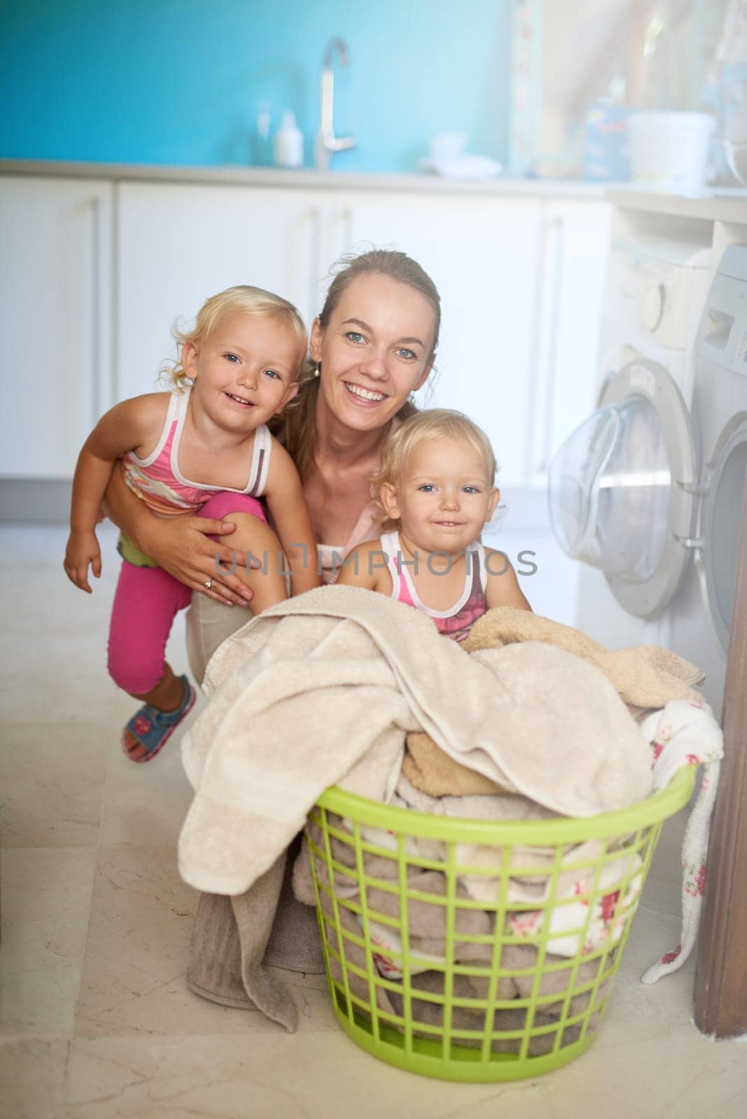 Mother, kids and portrait of girls, laundry and clothes in basket, washing machine and twins in home. House, woman and mom with babies, growth and development of children, happiness and apartment by YuriArcurs