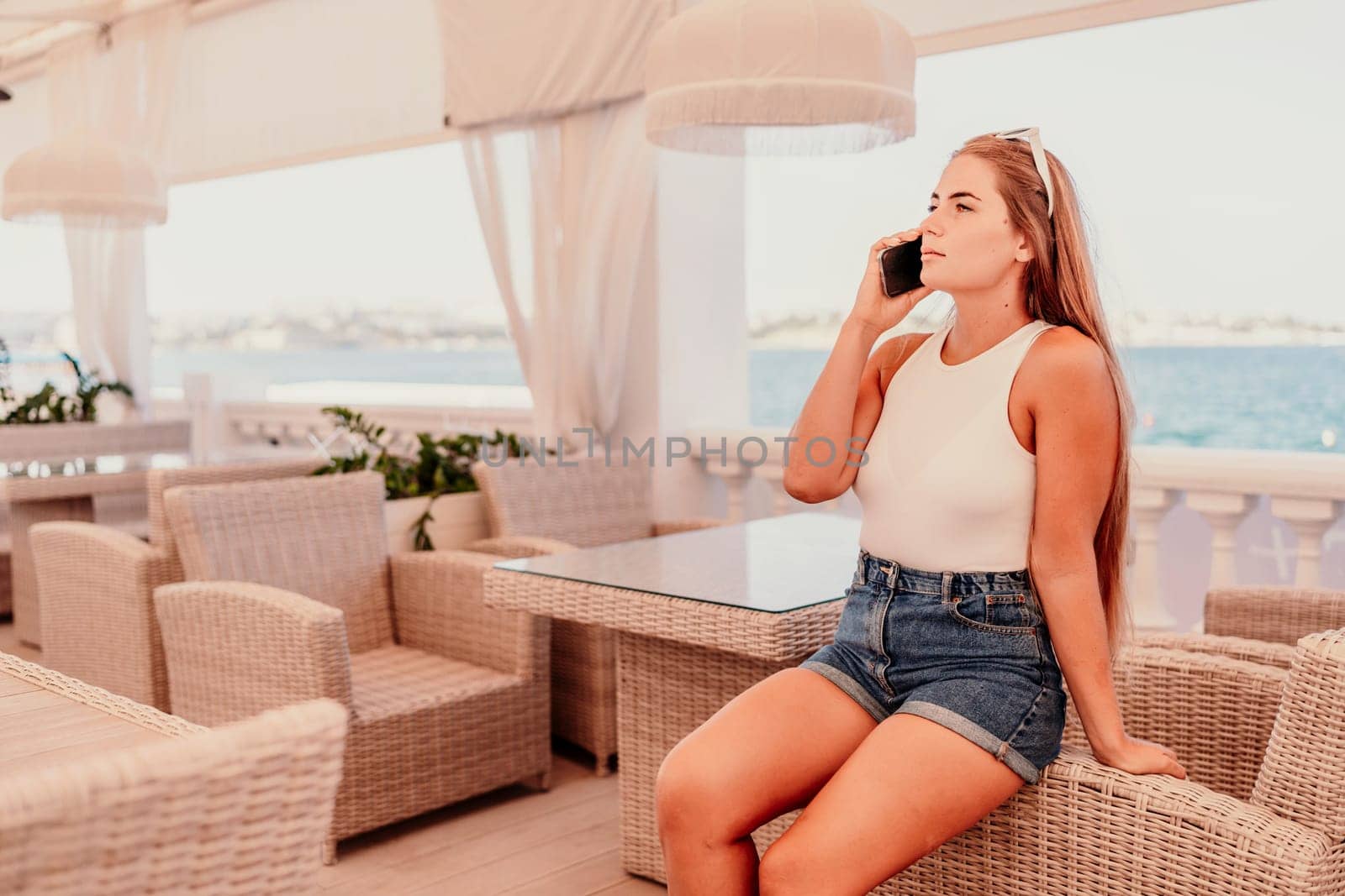 Cafe woman sitting at a table with a cell phone in her hand. She is looking at the screen and she is focused on her phone. The scene takes place in a restaurant or cafe, with multiple chairs. by Matiunina