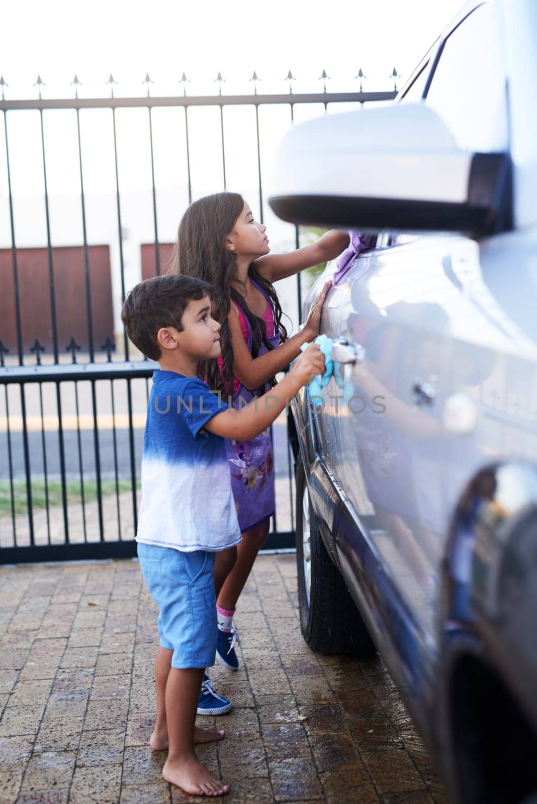 Children, car wash and helping siblings or outdoor together for to do list, discipline or teamwork. Boy, girl and cloth at transport in home driveway for cleaning responsibility, learning or task by YuriArcurs