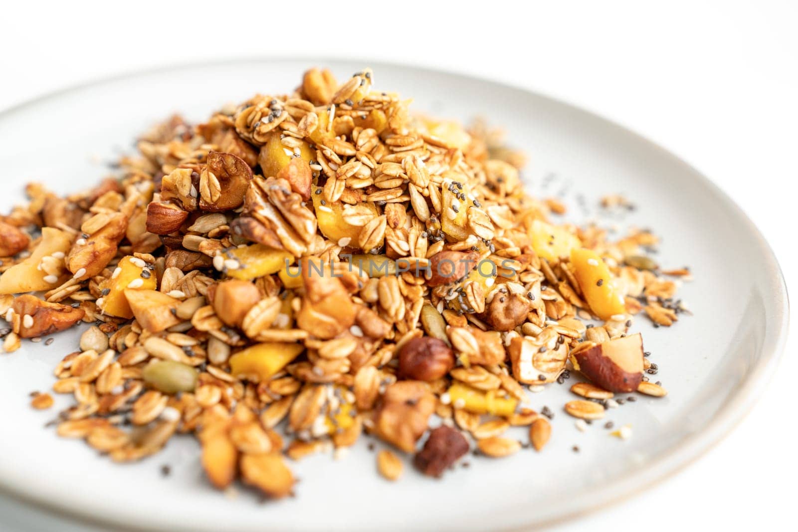 A bowl of granola with nuts and seeds on a white plate. The granola is a mix of different types of grains and nuts, and it looks like a healthy snack. by Matiunina