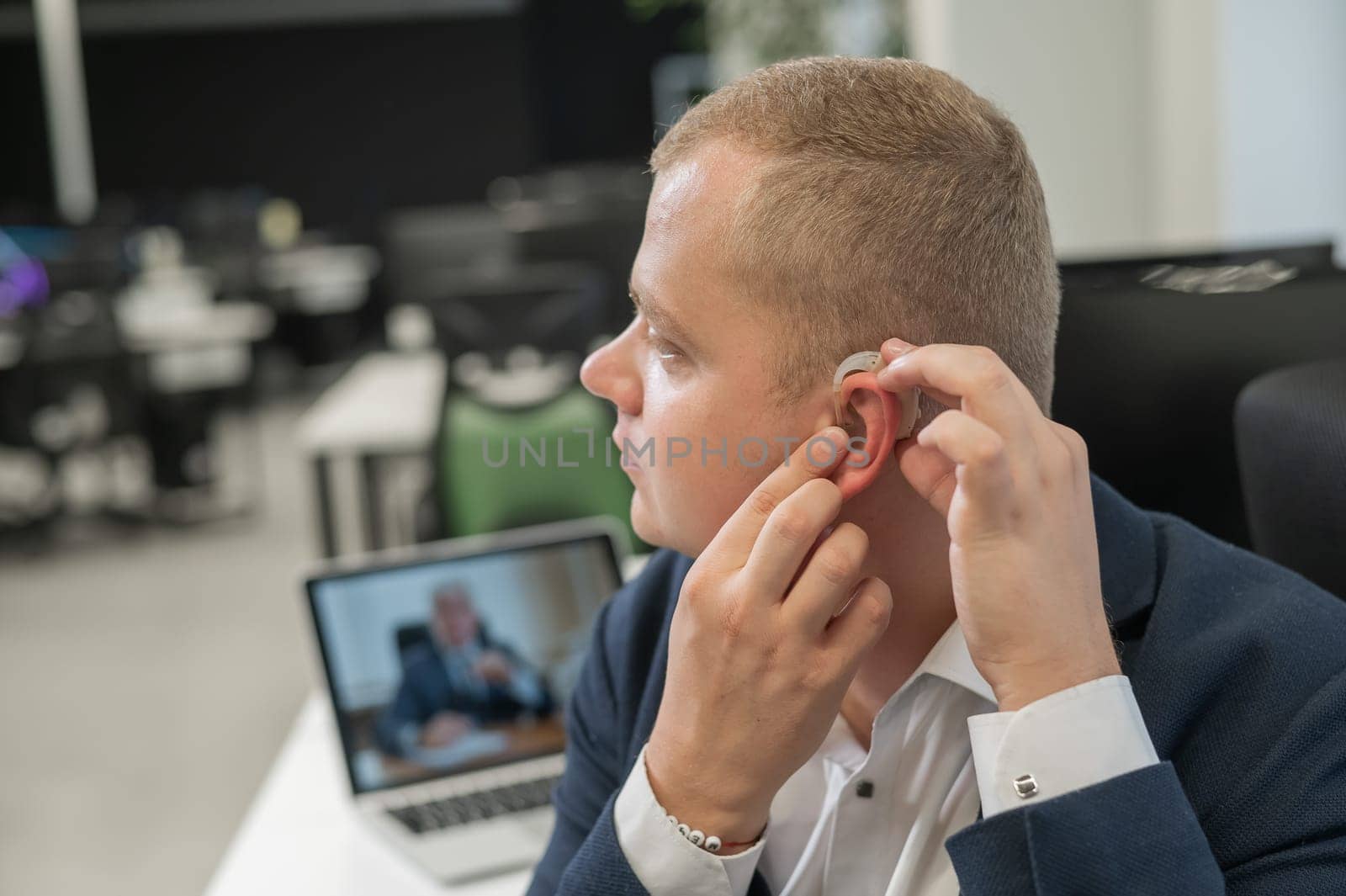 Caucasian man putting on hearing aid to online meeting on laptop