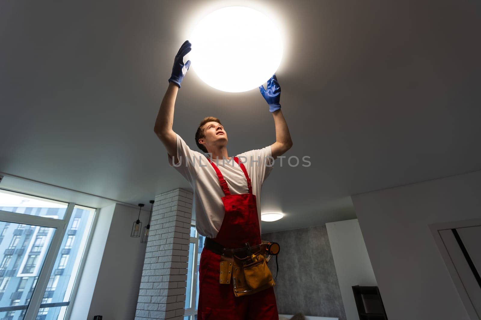 Electrician at work. Service for the repair of electrical wiring and replacement of ceiling lamps. A builder is installing a loft-style wooden ceiling. Rent-a-gent helps with the housework by Andelov13