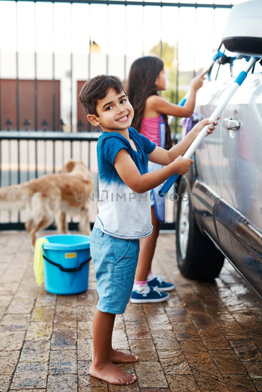 Children, portrait and home and washing car, kids and cleaning motor vehicle with equipment for fun. Siblings, driveway and helping with responsibility together on weekend, happy in outdoor for chore by YuriArcurs