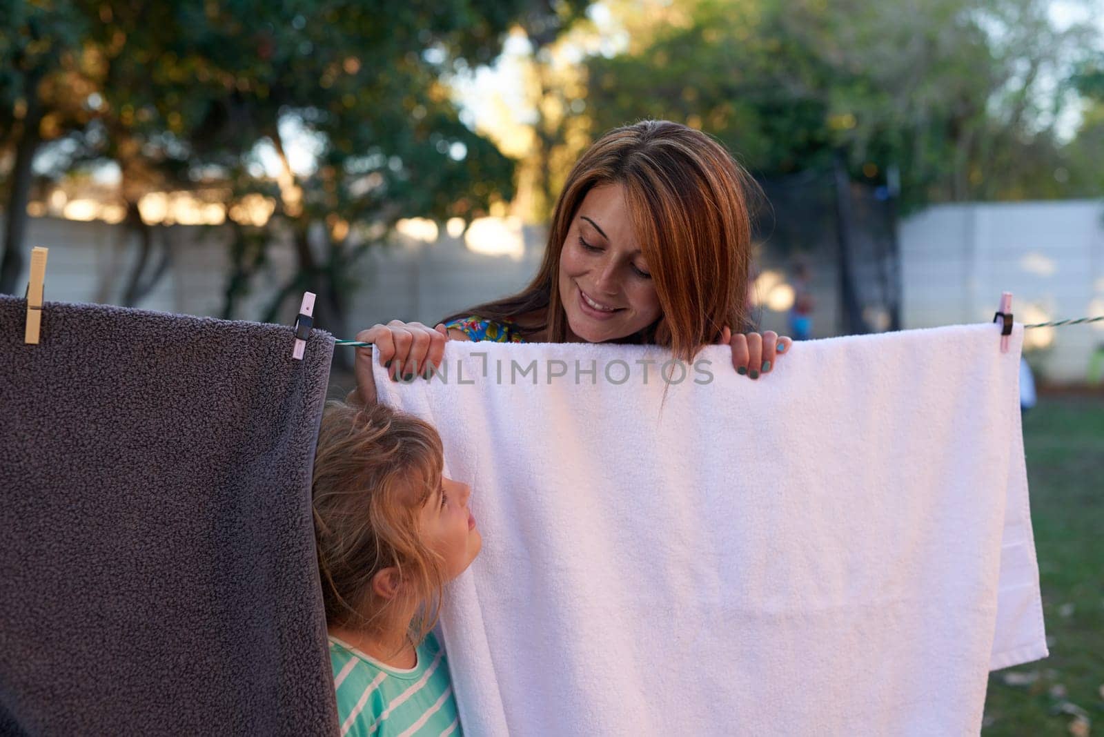 Hang, washing and mother in backyard with child in sunlight, wind and outdoors to dry. Housekeeping, family and mom with boy with laundry, towels and fabric on line for cleaning, wellness or hygiene by YuriArcurs