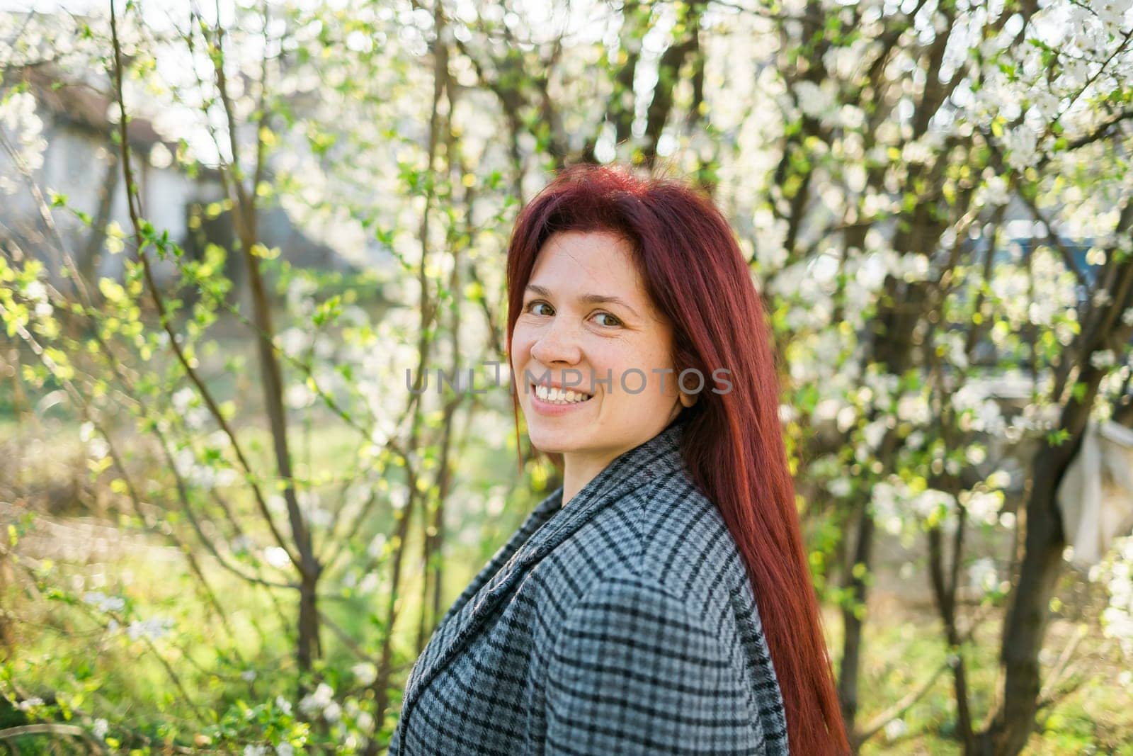 Beautiful red-haired woman enjoying smell in a flowering blooming spring garden. Spring blossom.