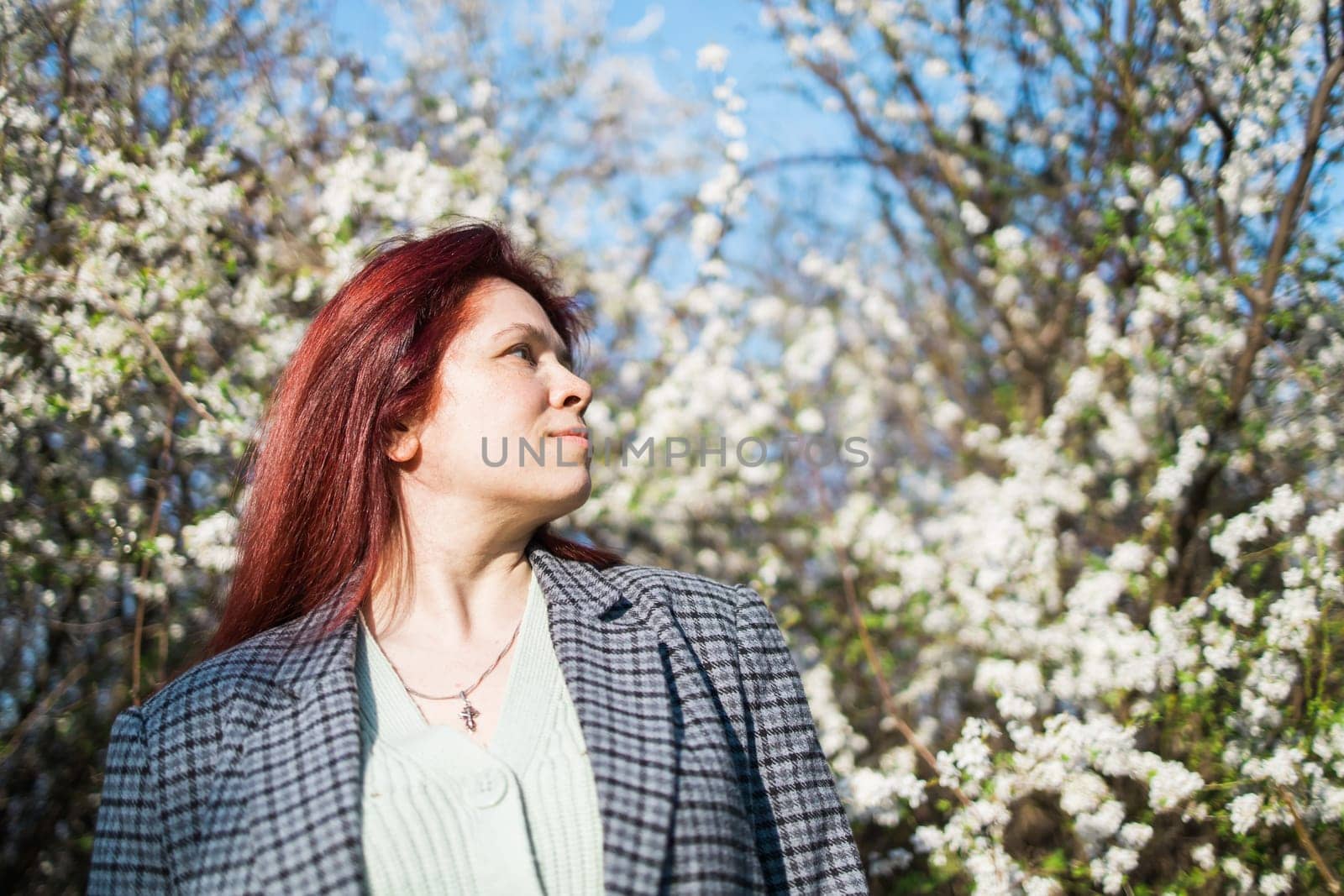 Beautiful red-haired woman enjoying smell in a flowering blooming spring garden. Spring blossom.