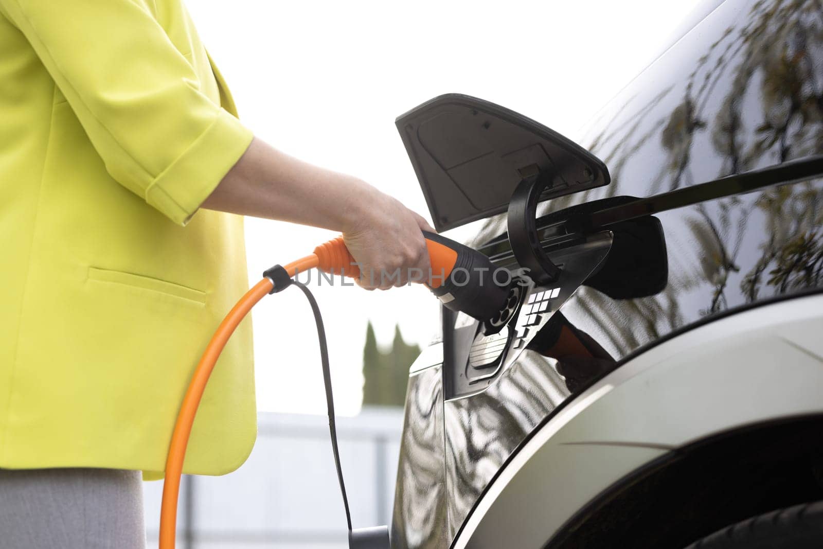 Woman's hands unplugging her electric automobile and closing the hatch in front of her home. Female unplugging the power supply cable from an white electric car