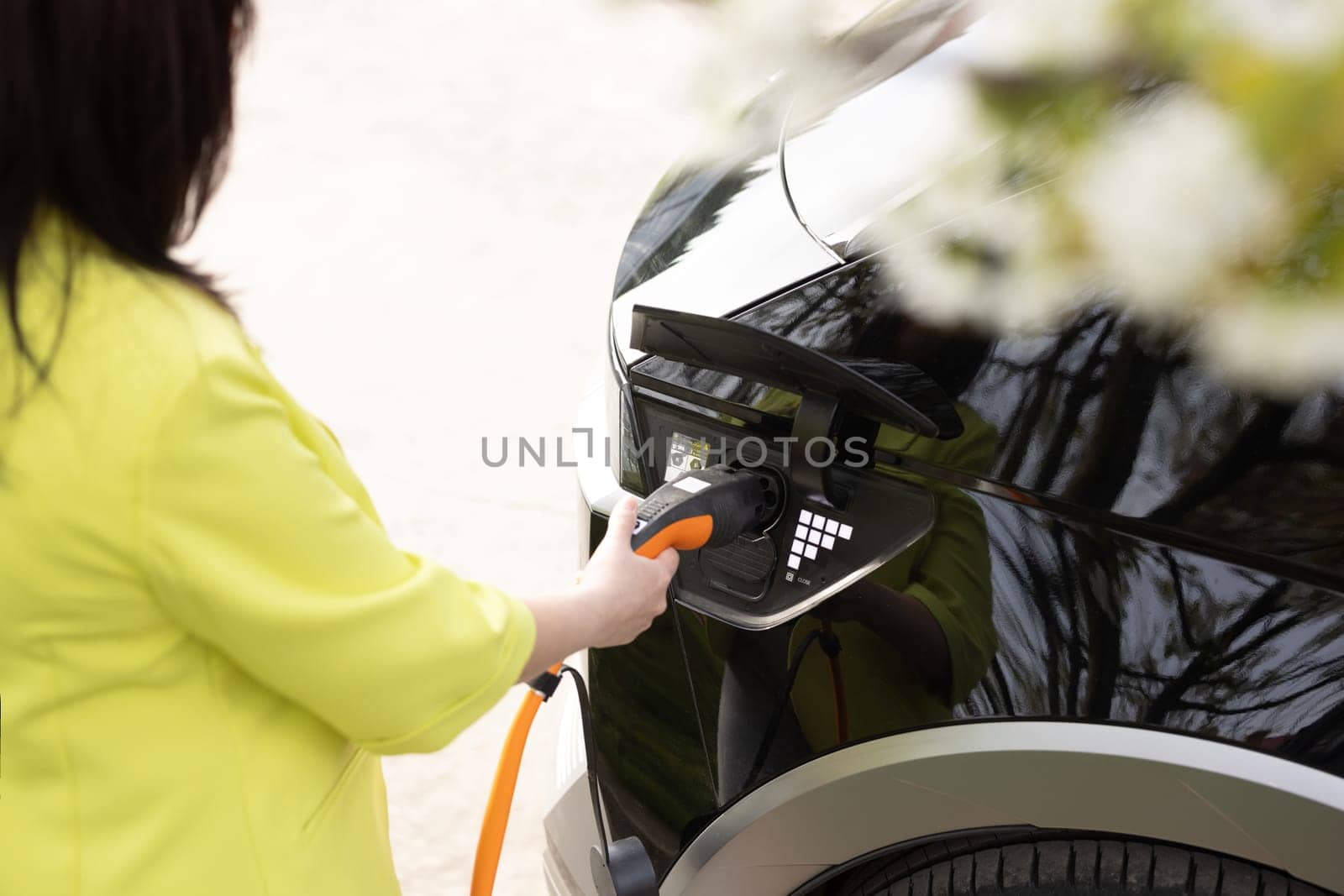 Unrecognizable female unplugging electric car cable. Woman hands disconnects plug power cable to charge electric car. Eco friendly alternative energy green environment concept.