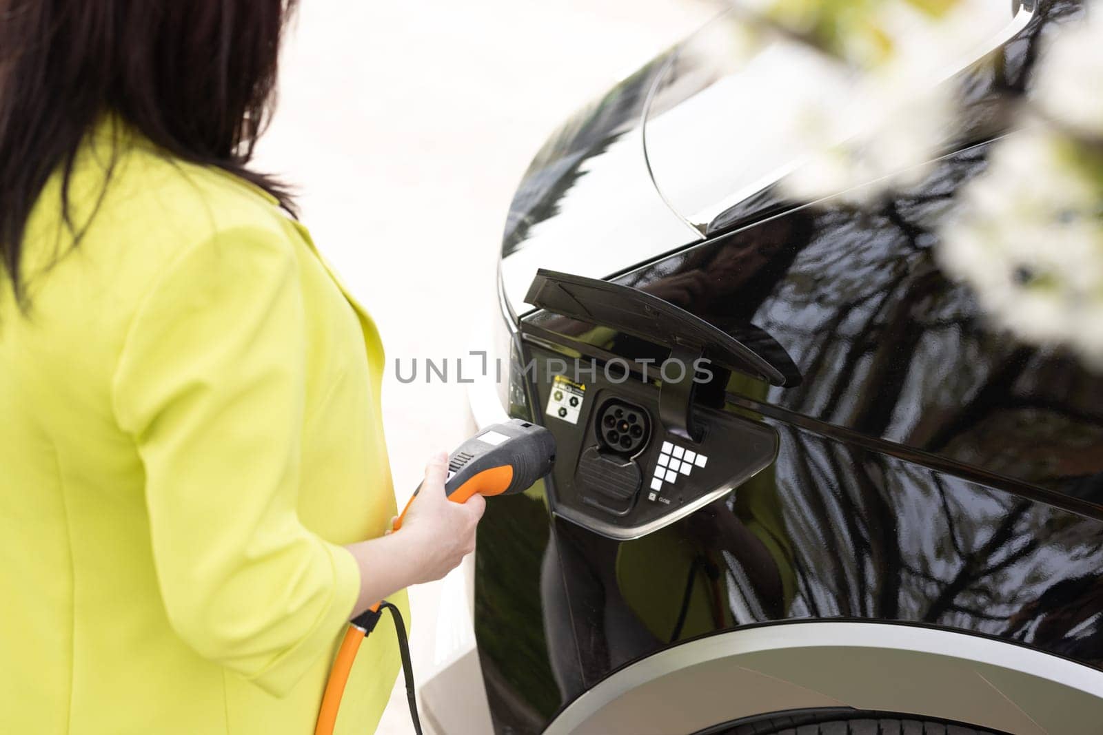 Female unplugging electric car cable and closing the hatch in front of her home. Woman hands disconnects plug power cable to charge electric car. Unplugging electric car charger by uflypro