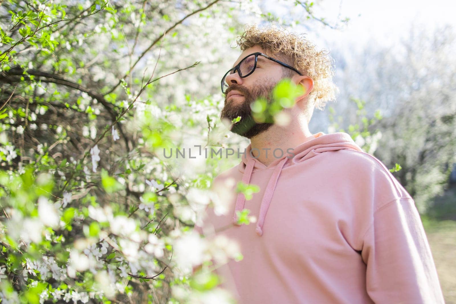 Male bearded man standing under branches with flowers of blooming almond or cherry tree in spring garden. Spring blossom. Copy space by Satura86
