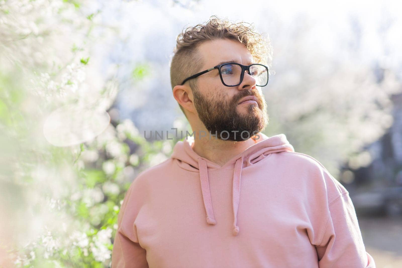 Male bearded man standing under branches with flowers of blooming almond or cherry tree in spring garden. Spring blossom. Copy space by Satura86