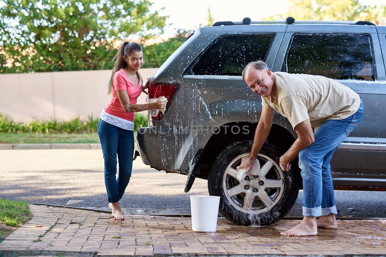 Portrait, family and washing car with soap, cloth and quality time on driveway. Cleaning transport, outdoor and face of father with young daughter with water, barefoot together and weekend chores.